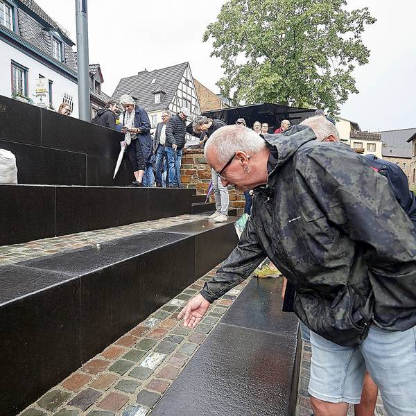 Ein Mann mit einer Regenjacke steht an einer Treppe, die zu einem kleinen Fluss führt.