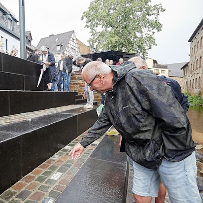 Ein Mann mit einer Regenjacke steht an einer Treppe, die zu einem kleinen Fluss führt.
