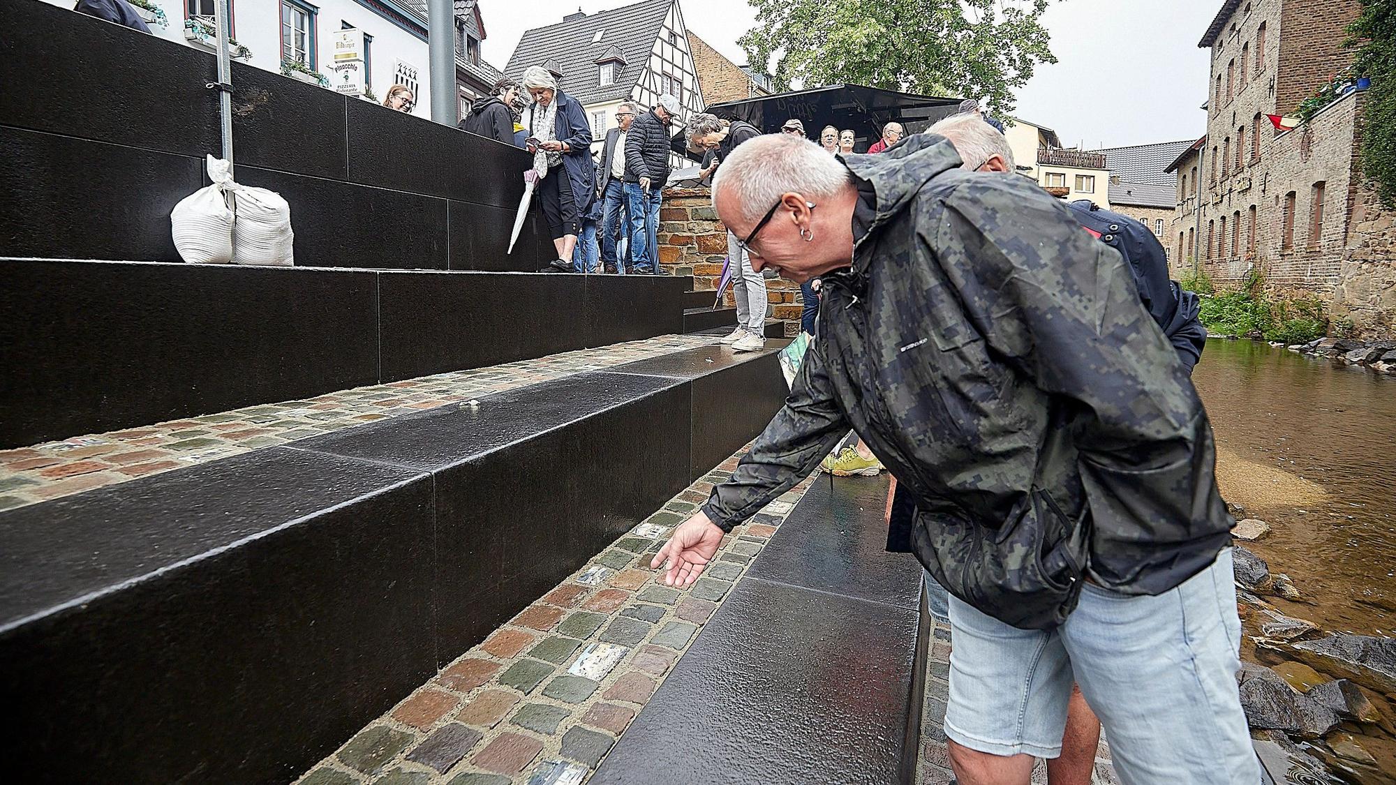 Ein Mann mit einer Regenjacke steht an einer Treppe, die zu einem kleinen Fluss führt.