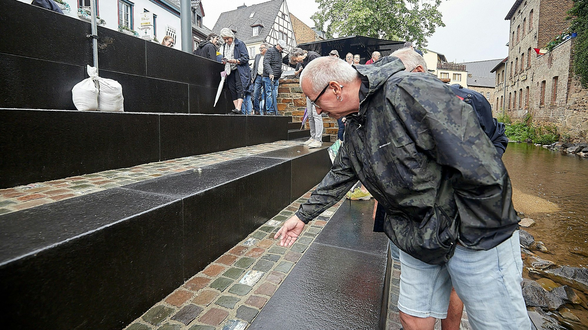 Ein Mann mit einer Regenjacke steht an einer Treppe, die zu einem kleinen Fluss führt.
