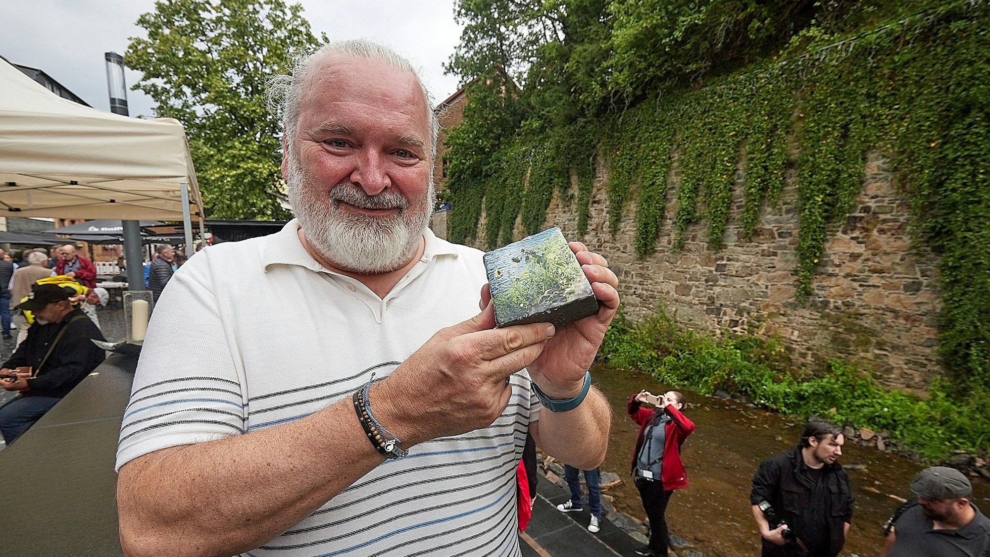 Ein Mann präsentiert einen Pflasterstein, der mit einem Foto bedruckt ist.