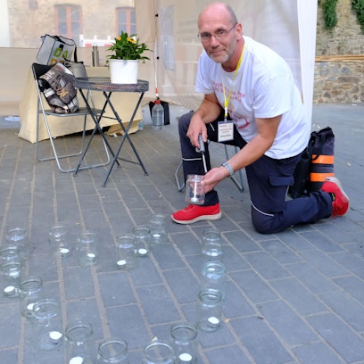 Ein Mann kniet auf der Straße und zündet eine Kerze in einem Glas an.