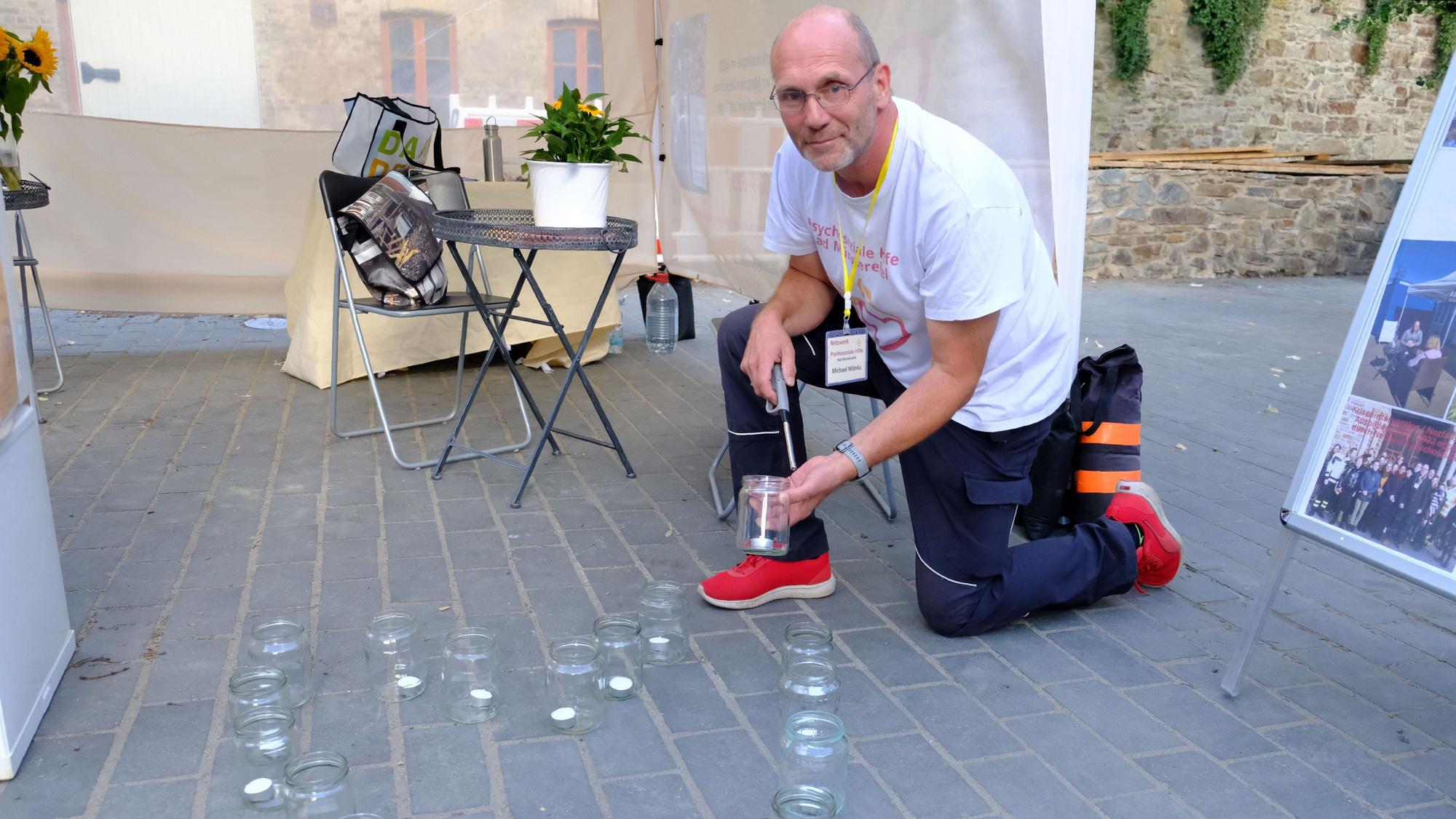 Ein Mann kniet auf der Straße und zündet eine Kerze in einem Glas an.