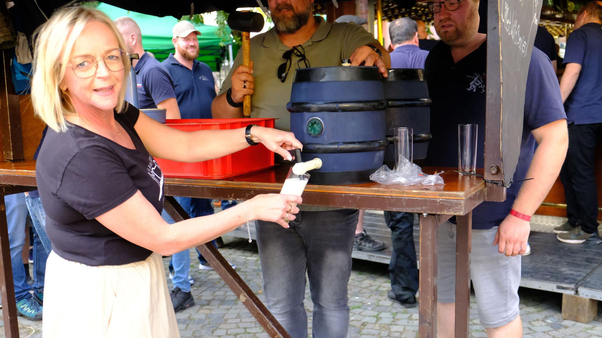 Eine Frau zapft ein Glas Kölsch aus einem kleinen Bierfass.
