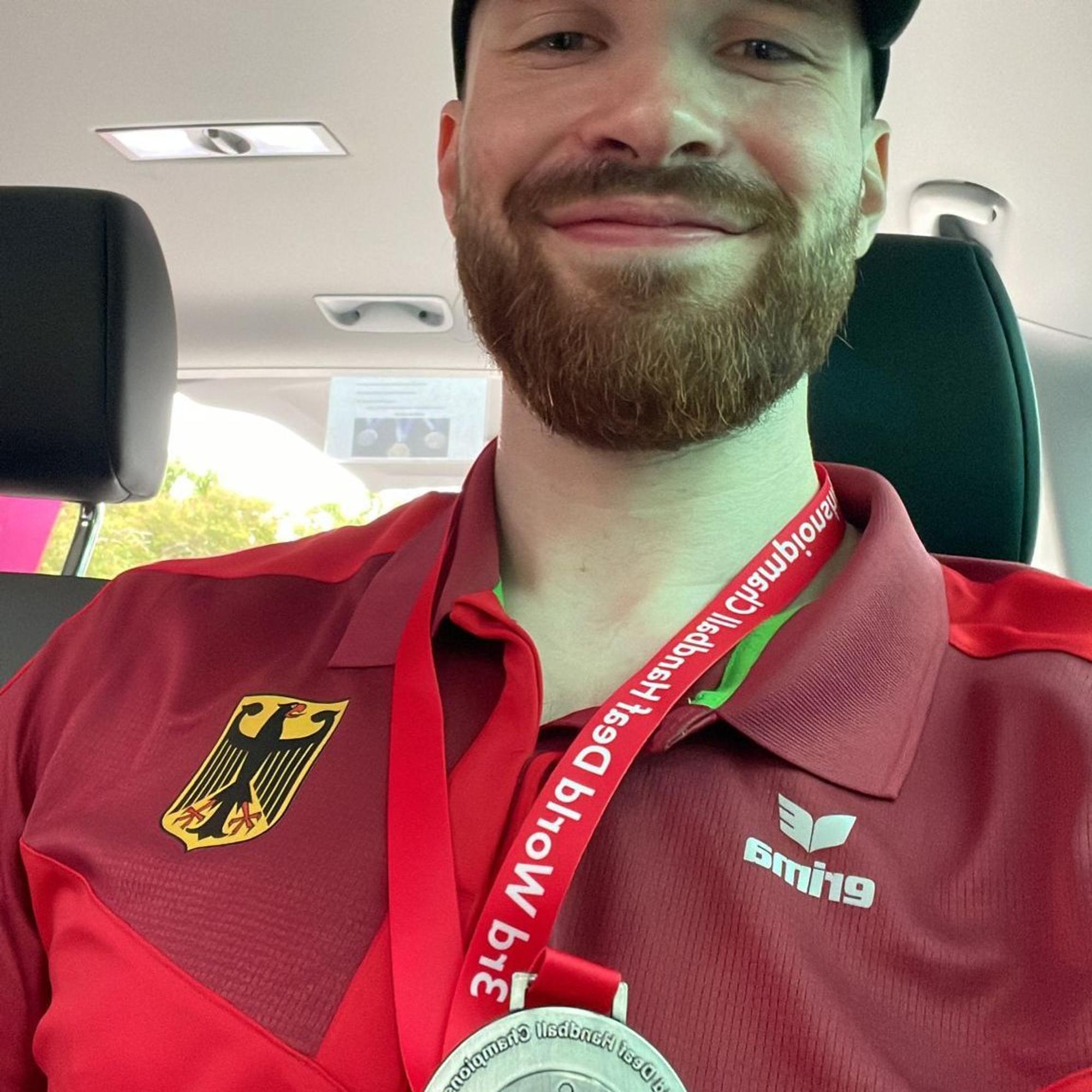 Simon Schöller lächelt und hält die Silbermedaille in die Kamera.