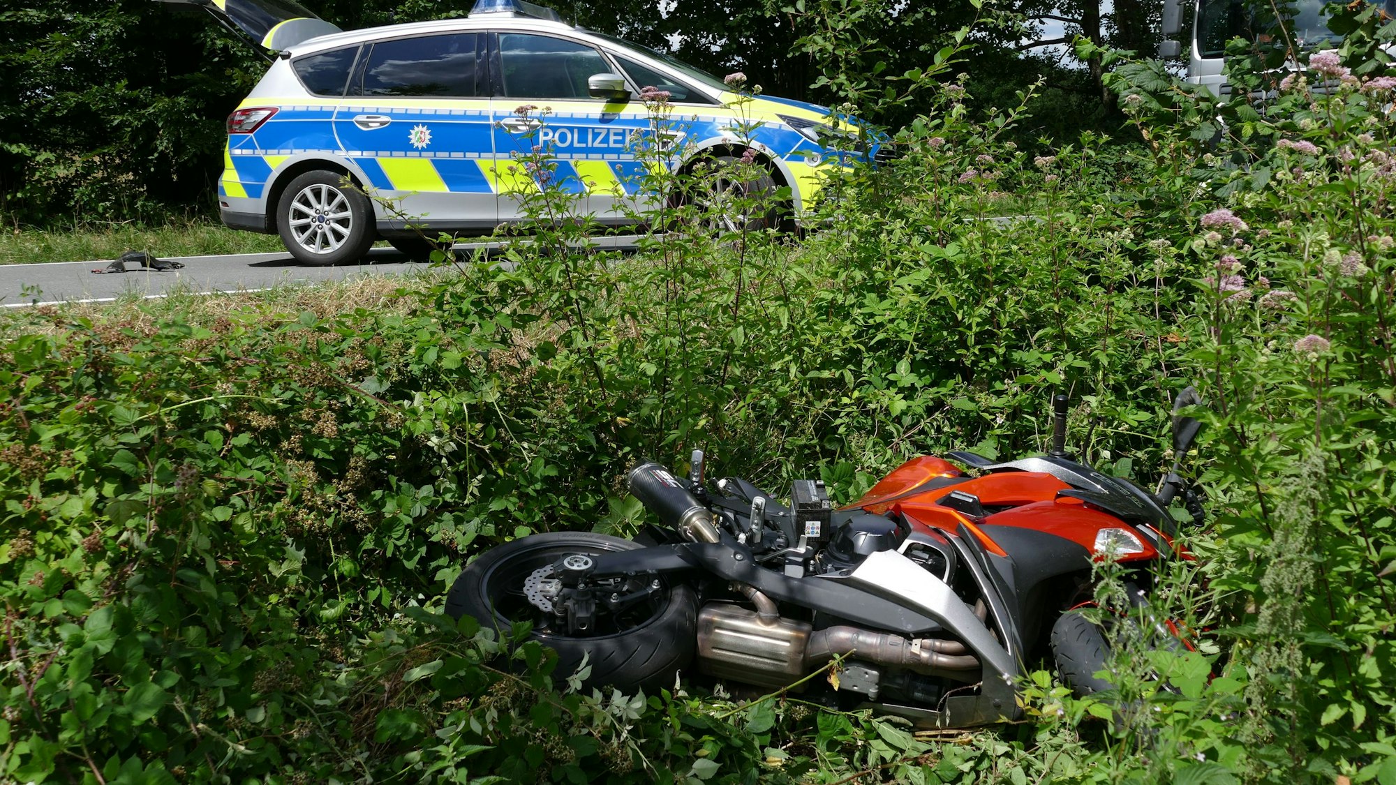 Ein Motorrad liegt in einem Straßengraben. Auf der Straße steht ein Polizeiauto.