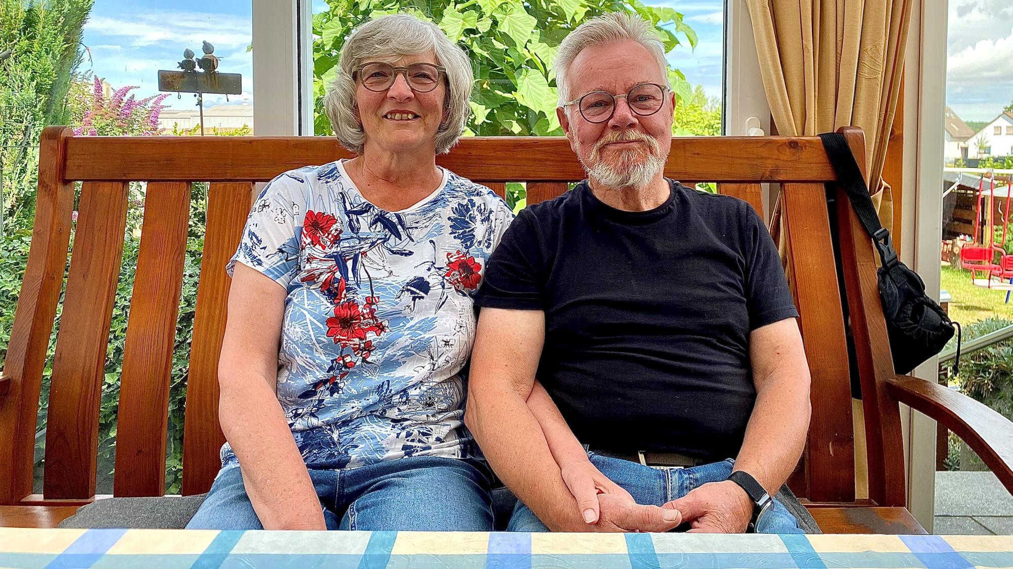 Ein Mann und eine Frau sitzen auf einer Bank an einem Tisch und halten sich bei den Händen.