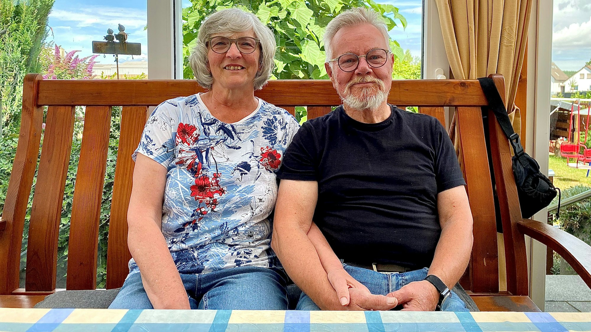 Ein Mann und eine Frau sitzen auf einer Bank an einem Tisch und halten sich bei den Händen.