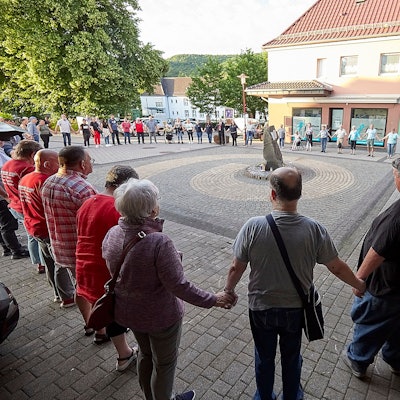 Zahlreiche Menschen stehen in einem großen Kreis um einen Stein. Sie halten sich zum stillen Gedenken an den Händen.