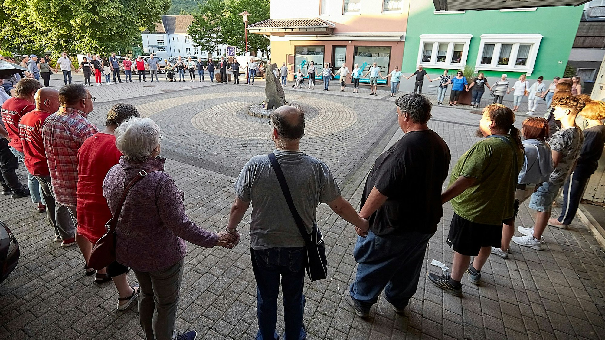 Zahlreiche Menschen stehen in einem großen Kreis um einen Stein. Sie halten sich zum stillen Gedenken an den Händen.