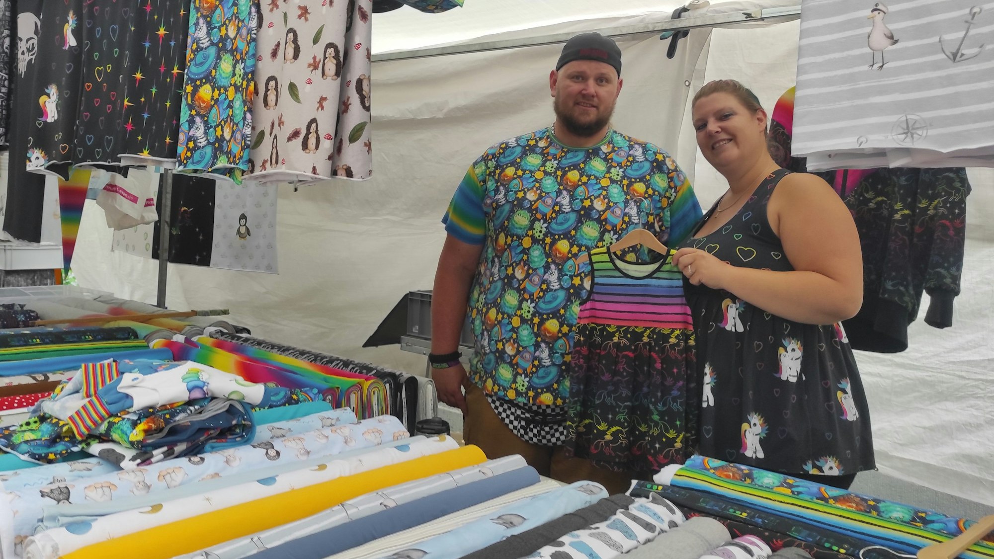 Ein Mann und eine Frau stehen hinter einem Stand für Stoffe.