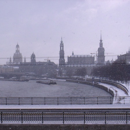 Aus dem Zugfenster ist in dichtem Schneetreiben das Elbpanorama von Dresden zu erkennen.