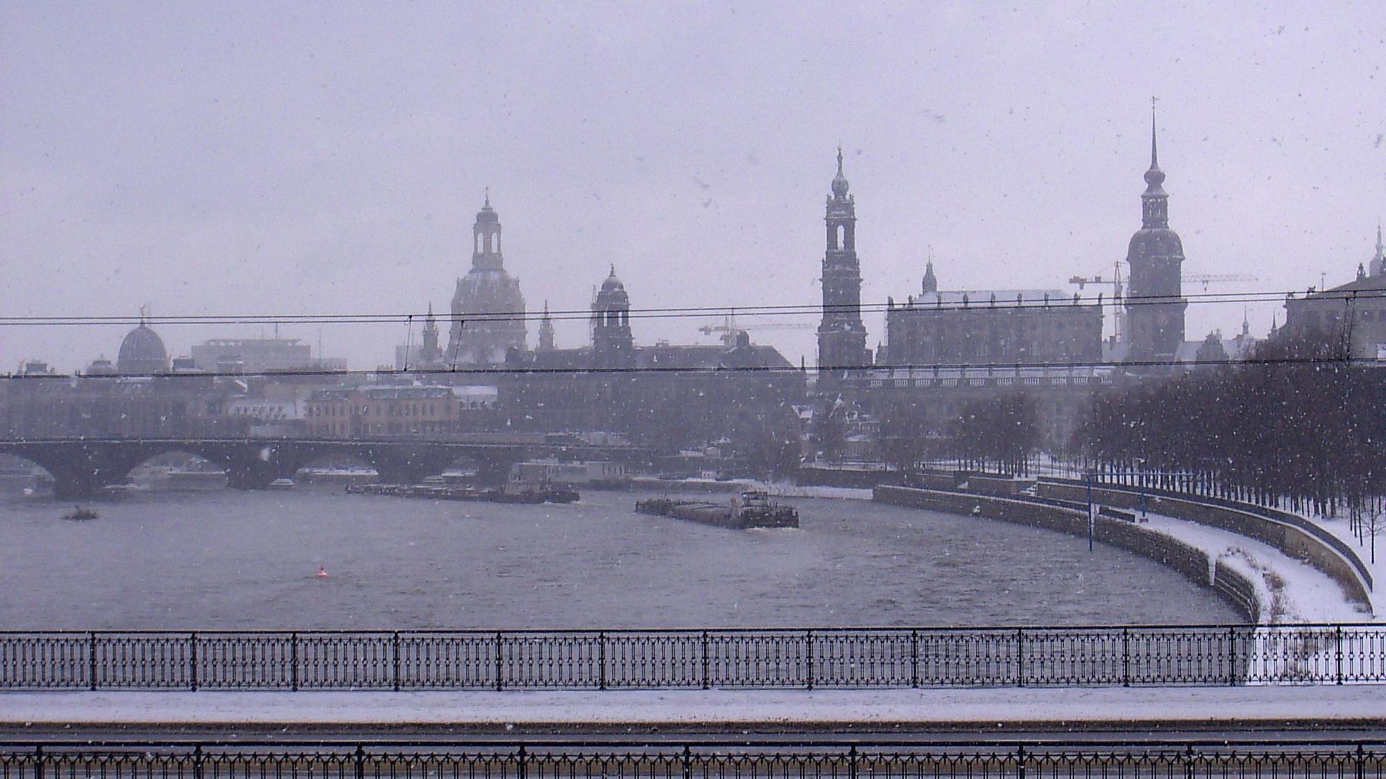 Aus dem Zugfenster ist in dichtem Schneetreiben das Elbpanorama von Dresden zu erkennen.