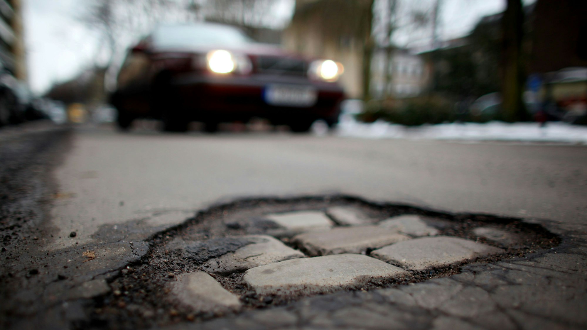 Ein Auto fährt auf ein Schlagloch in der Fahrbahndecke einer Straße in Köln zu.
