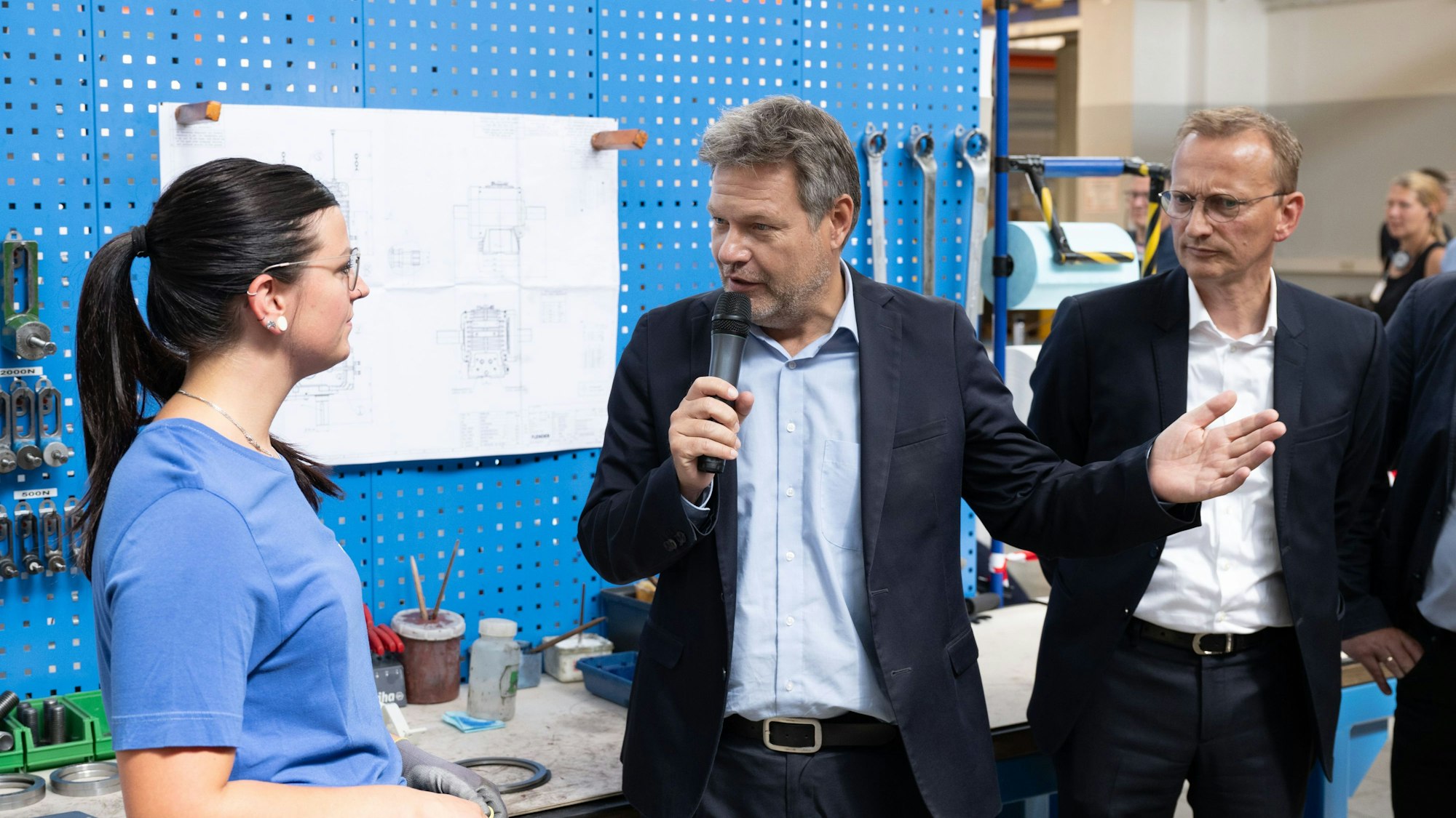 Robert Habeck (M, Bündnis 90/Die Grünen), Bundesminister für Wirtschaft und Klimaschutz, steht zum Abschluss seiner Sommerreise in einer Werkhalle der Flender Industriegetriebe GmbH neben Andreas Evertz (r), CEO von Flender, und spricht mit einer Mitarbeiterin.