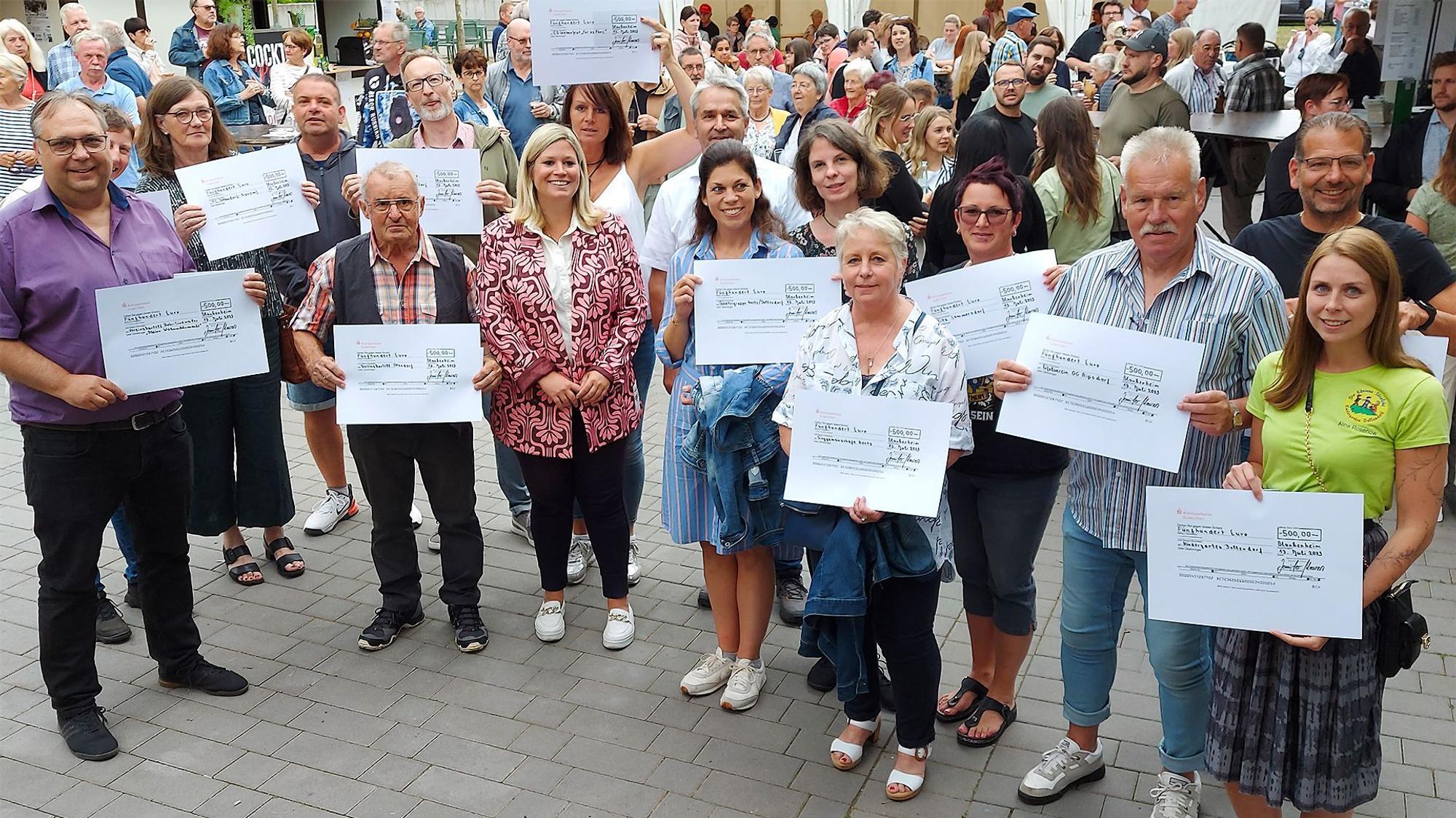 Zahlreiche Menschen stehen zusammen. Einige halten großformatige Spendenschecks in die Höhe.