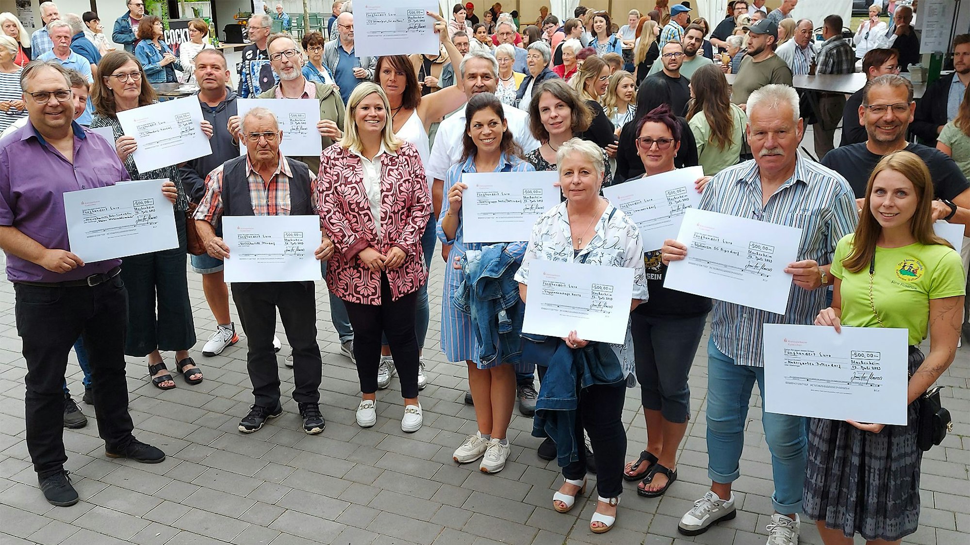 Zahlreiche Menschen stehen zusammen. Einige halten großformatige Spendenschecks in die Höhe.