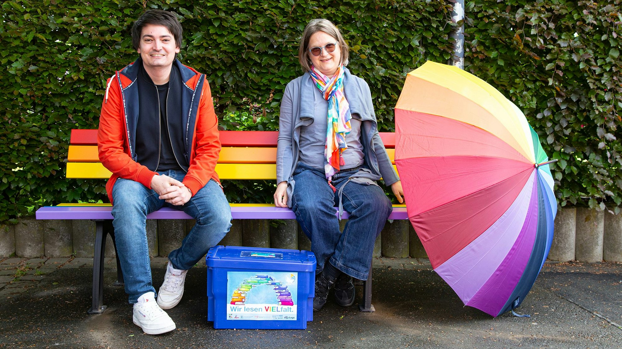 Ein Mann und eine Frau sitzen auf einer Parkbank in Regenbogenfarben.