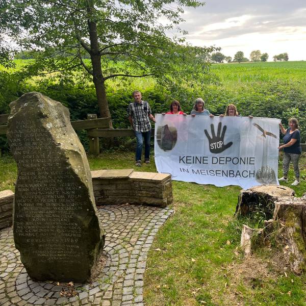 Fünf Menschen stehen mit einem Protestbanner auf einer Wiese.