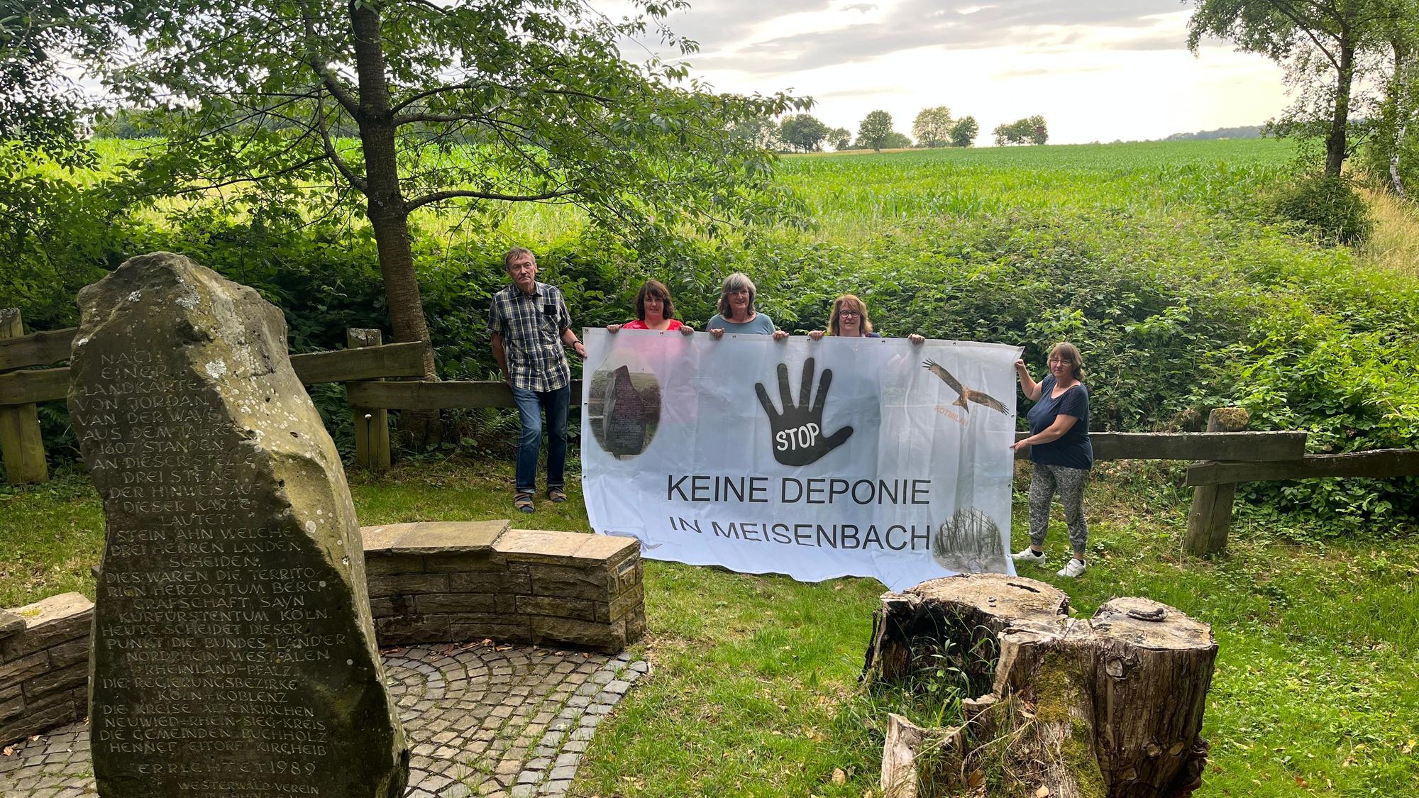 Fünf Menschen stehen mit einem Protestbanner auf einer Wiese.