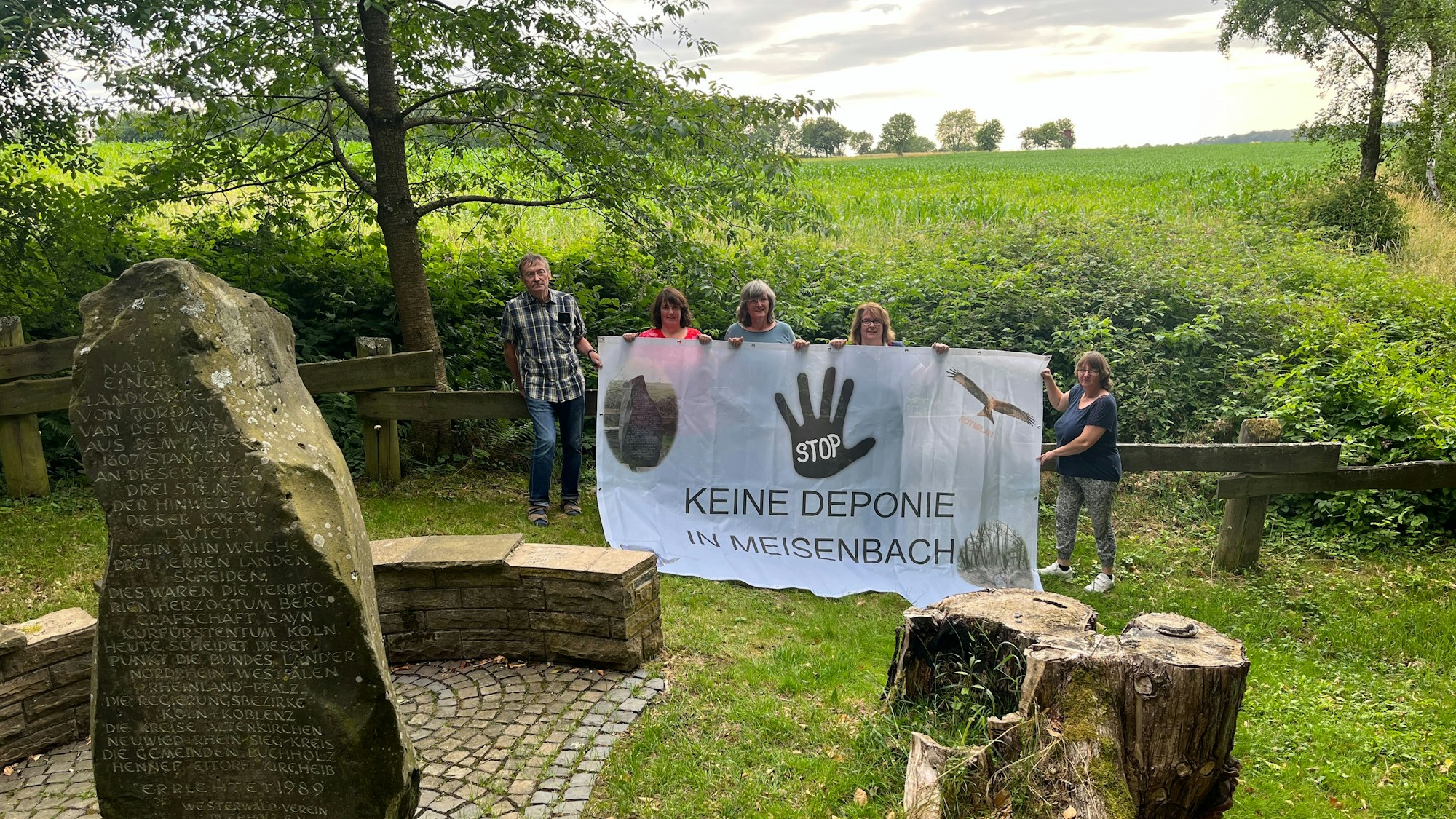 Fünf Menschen stehen mit einem Protestbanner auf einer Wiese.