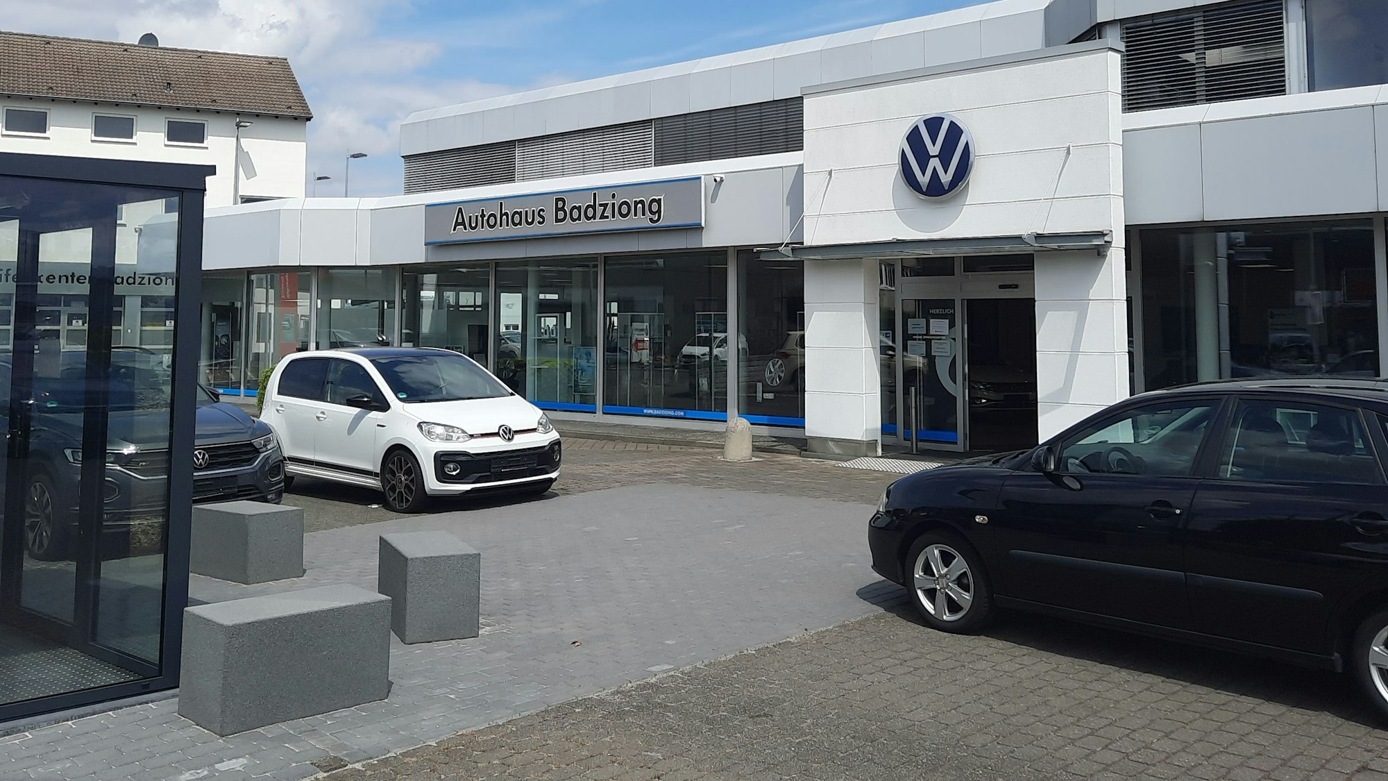 Der Eingang des Autohaus Badziong, drei Autos stehen davor auf dem Platz.