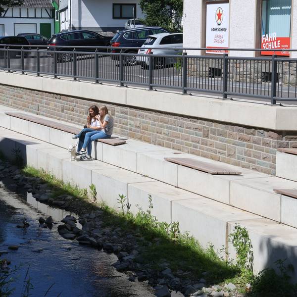 Zwei Mädchen sitzen an einer neu gestalteten Uferpromenade.