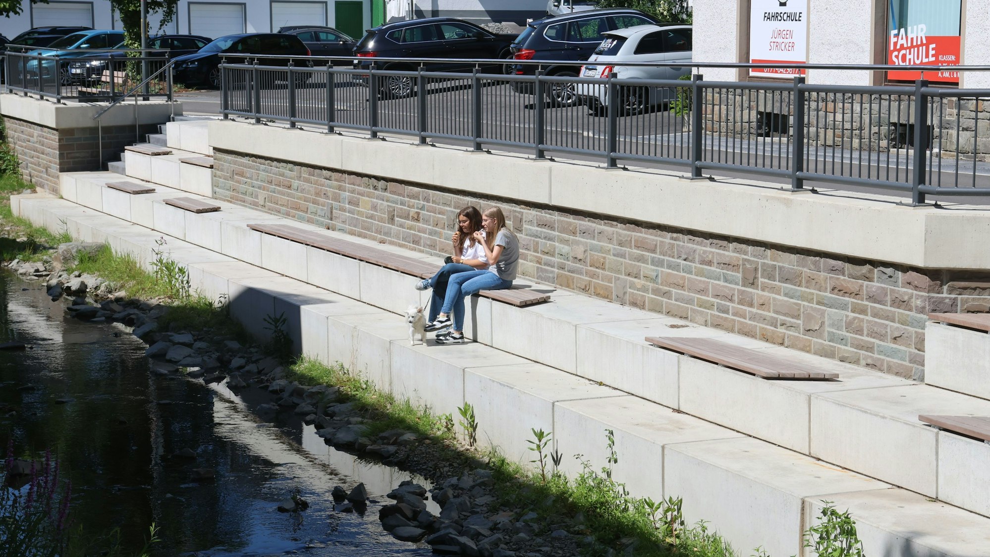 Zwei Mädchen sitzen an einer neu gestalteten Uferpromenade.