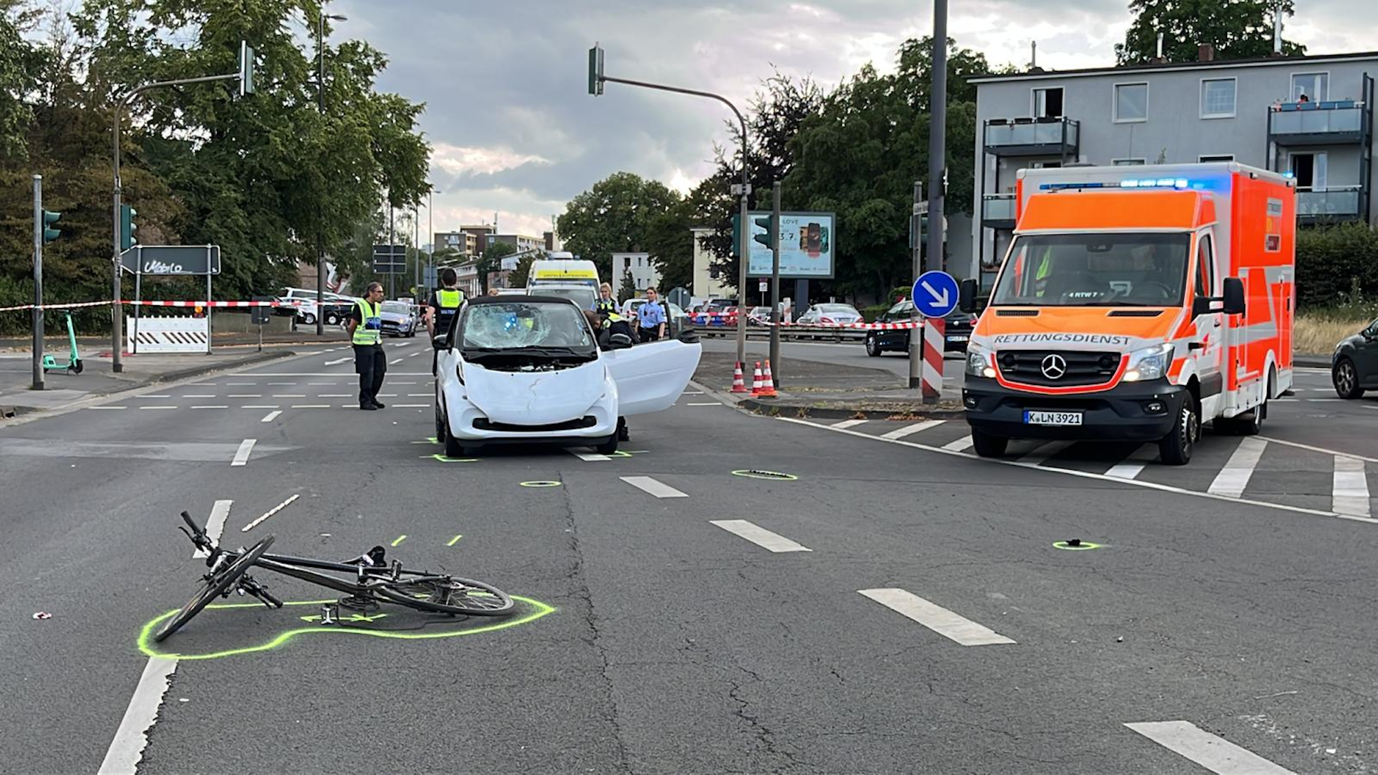 Unfallort mit einem demonlierten Auto, einem auf dem Boden liegenden Fahrrad und einem Krankenwagen