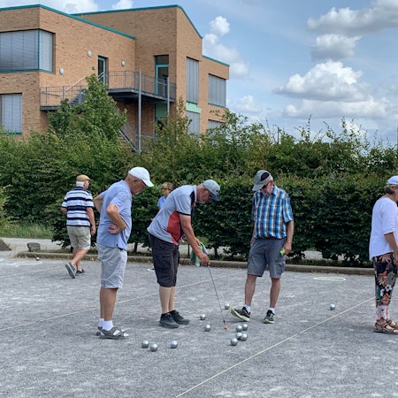Einige ältere Menschen stehen auf einer Boulebahn inmitten von Kugeln.