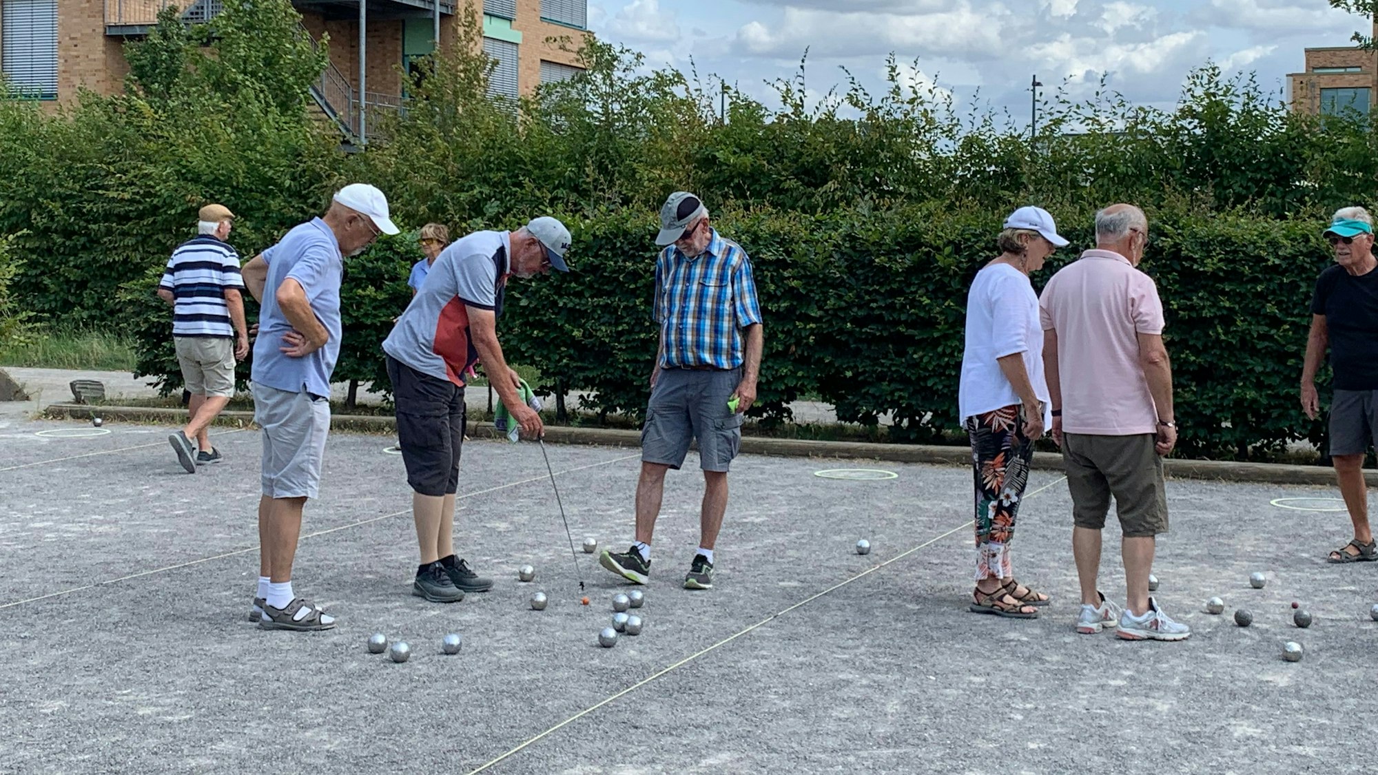 Einige ältere Menschen stehen auf einer Boulebahn inmitten von Kugeln.