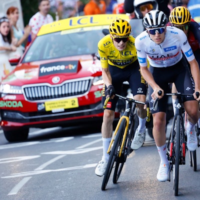 Der Slowene Tadej Pogacar in einem Anstieg bei der Tour de France vor dem Träger des Gelben Trikots, Jonas Vingegaard. Hinter ihnen fährt der Spanier Carlos Rodriguez, unmittelbar vor einem offiziellen Fahrzeug der Frankreich-Rundfahrt.