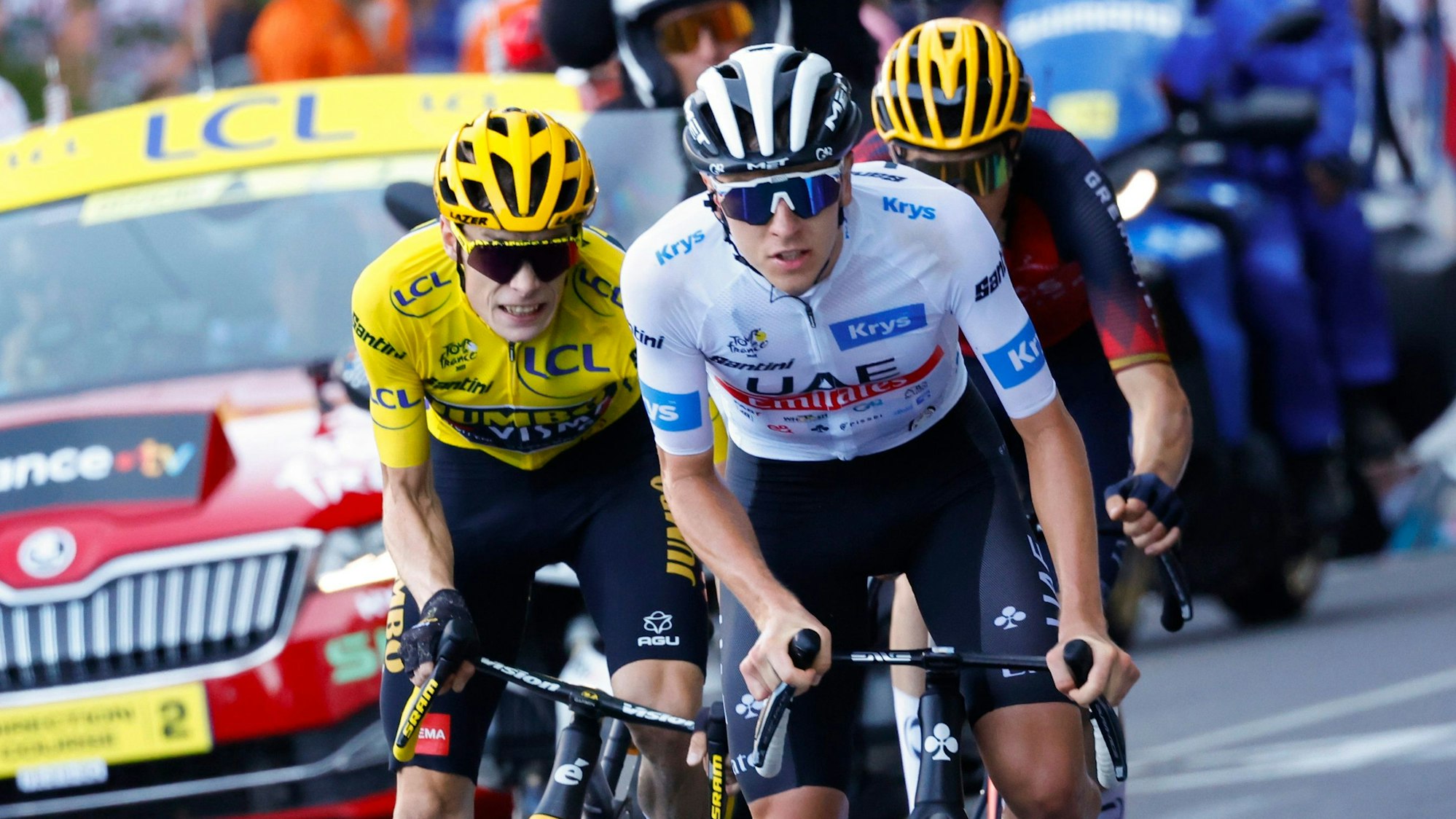 Der Slowene Tadej Pogacar in einem Anstieg bei der Tour de France vor dem Träger des Gelben Trikots, Jonas Vingegaard. Hinter ihnen fährt der Spanier Carlos Rodriguez, unmittelbar vor einem offiziellen Fahrzeug der Frankreich-Rundfahrt.