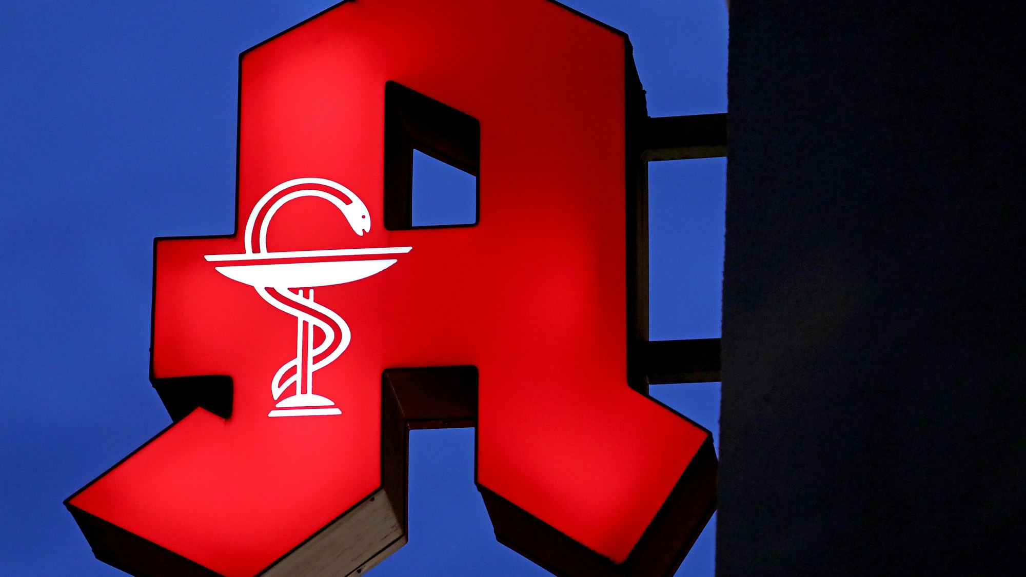 Das Apotheken-Logo leuchtet an einer Apotheke.