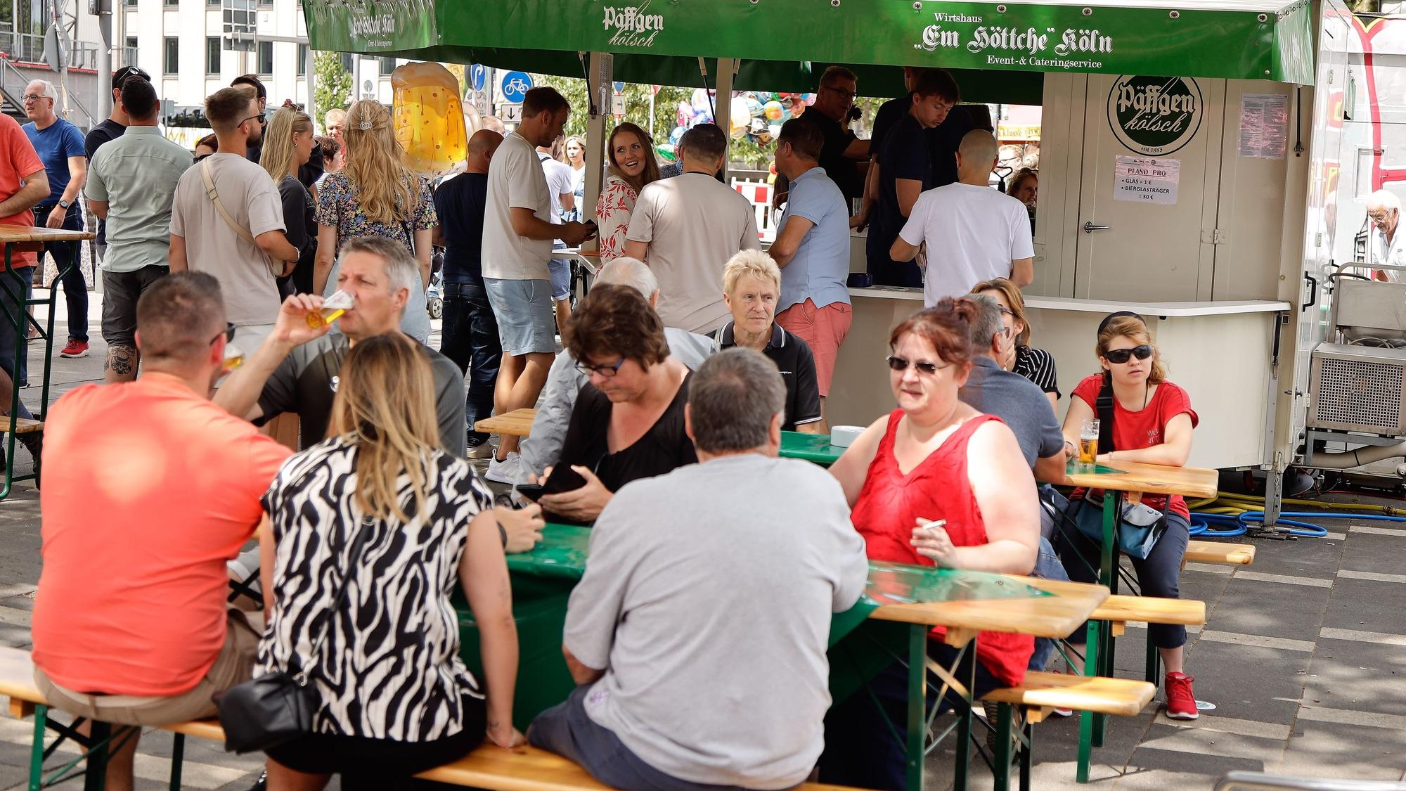 Menschen sitzen auf Bierbänken und trinken etwas.
