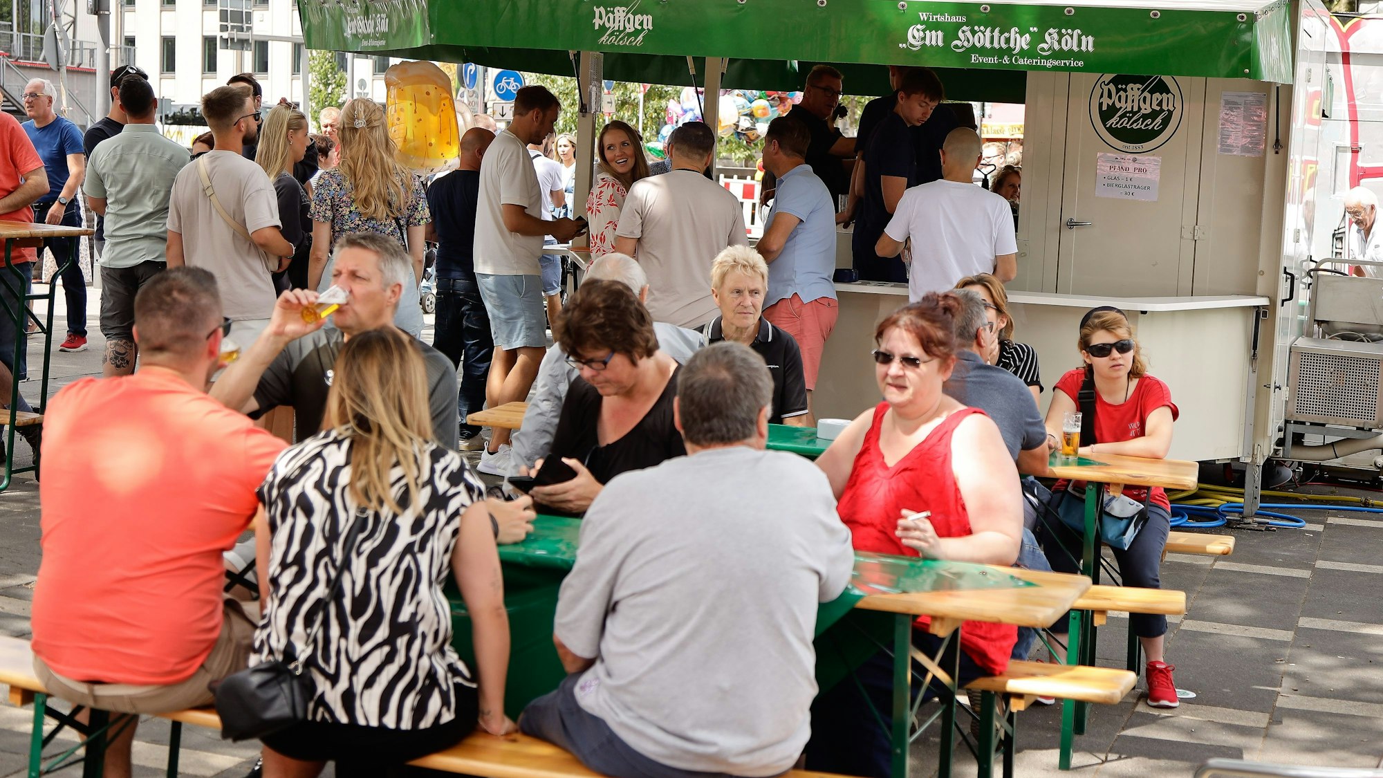Menschen sitzen auf Bierbänken und trinken etwas.