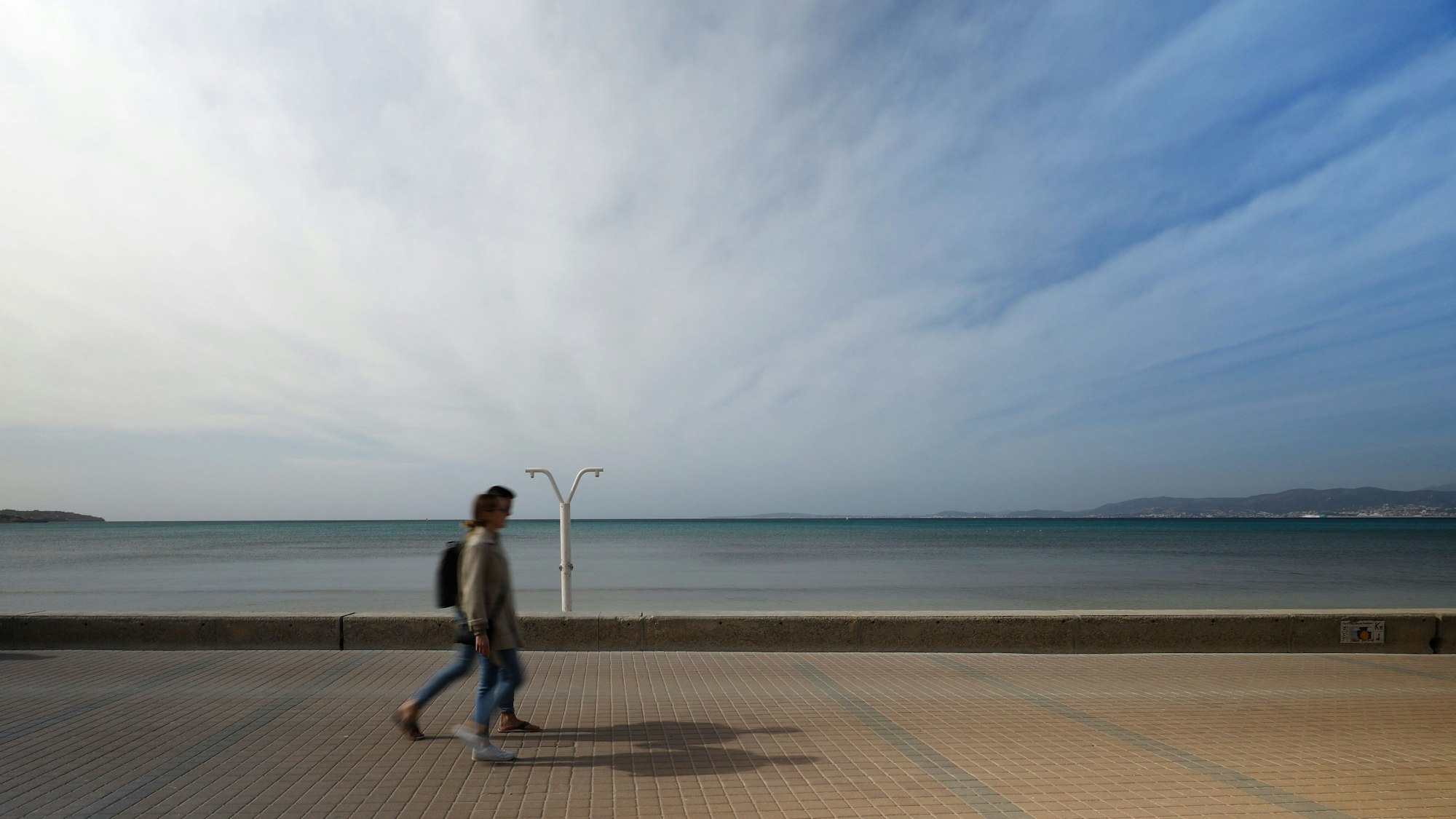 Menschen gehen an der Strandpromenade von Arenal auf Mallorca entlang.