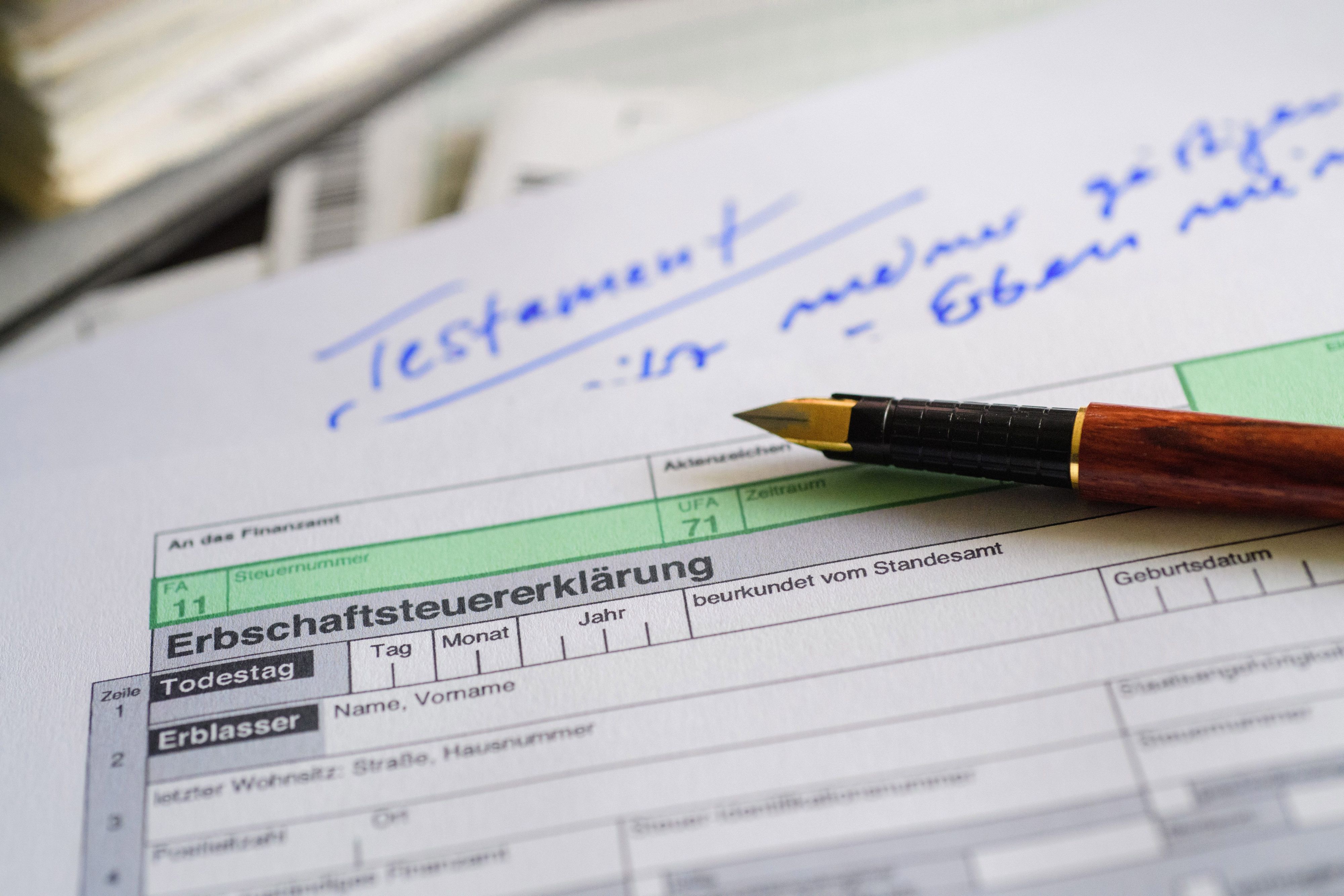 Ein Formular für die Erbschaftsteuererklärung sowie Stift und Testament liegen auf einem Tisch.