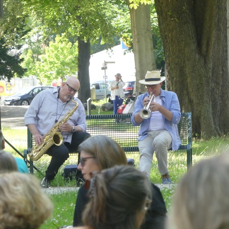 Bernd Delbrügge und Ebasa Pallada sitzen auf einer Bank und musizieren.