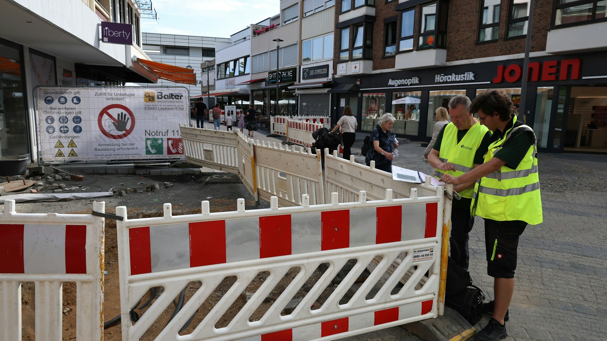 Die beiden Experten schauen an einer abgesperrten Baugruppe in eine Mappe mit Unterlagen.