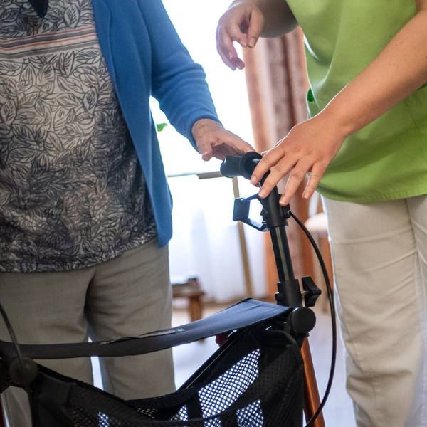 Eine Pflegefachkraft hilft einer Bewohnerin in einem Seniorenheim mit ihrem Rollator.