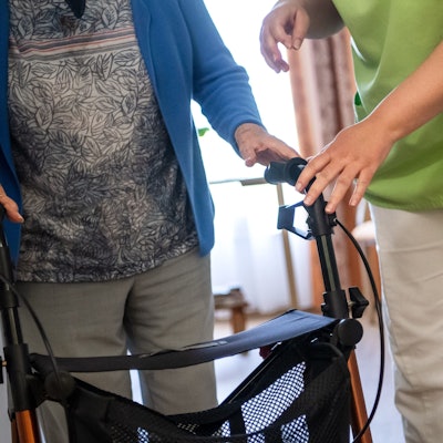 Eine Pflegefachkraft hilft einer Bewohnerin in einem Seniorenheim mit ihrem Rollator.