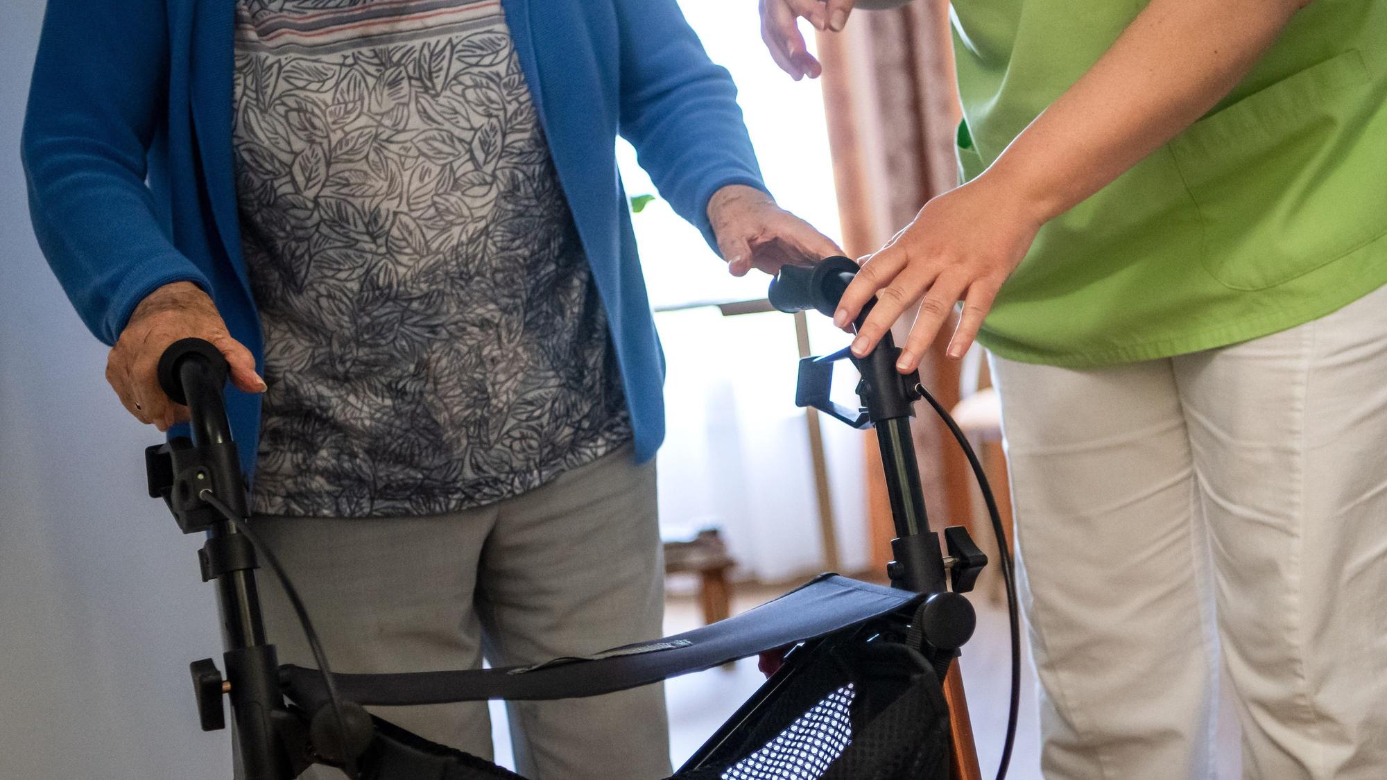 Eine Pflegefachkraft hilft einer Bewohnerin in einem Seniorenheim mit ihrem Rollator.