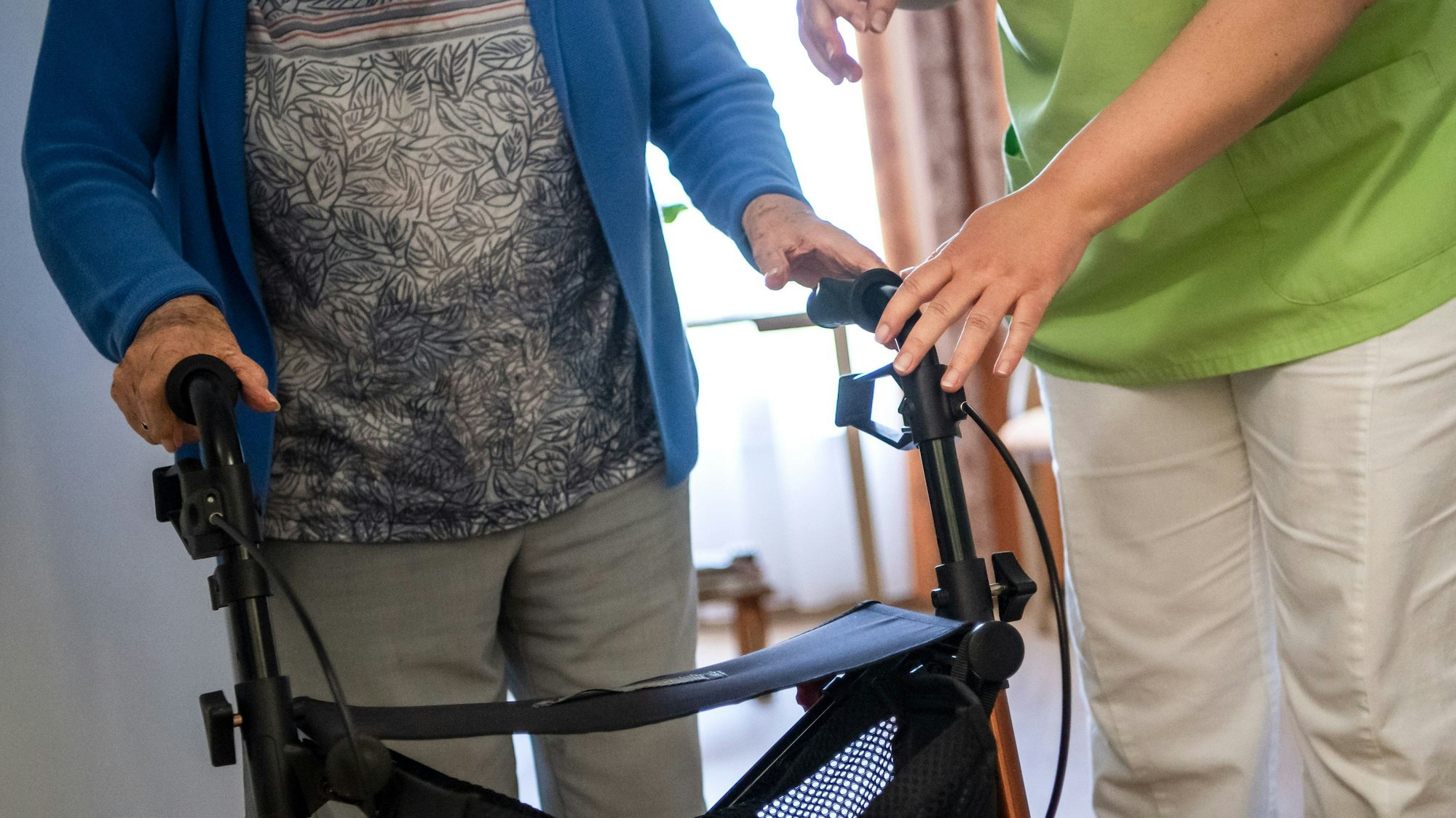Eine Pflegefachkraft hilft einer Bewohnerin in einem Seniorenheim mit ihrem Rollator.