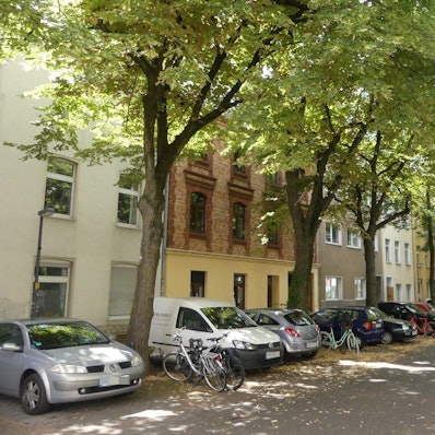 Eine Straße in Ehrenfeld mit Bäumen und geparkten Autos.
