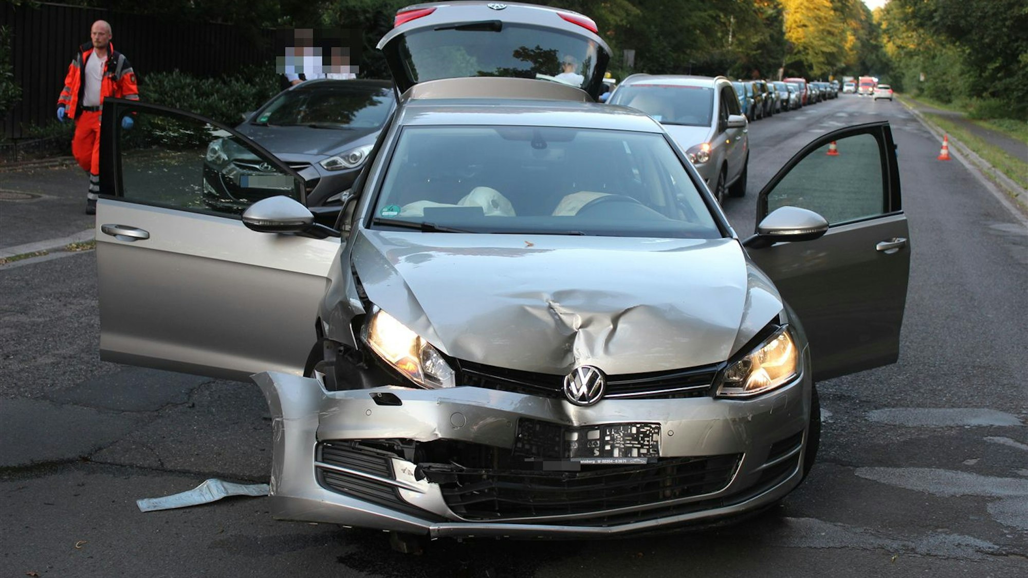 Ein VW mit verbeulter Motorhaube steht auf einer Straße. Im Hintergrund geht ein Rettungsdienstmitarbeiter.