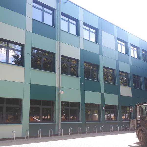 Ein grüner Schulbau mit einem Bagger davor.
