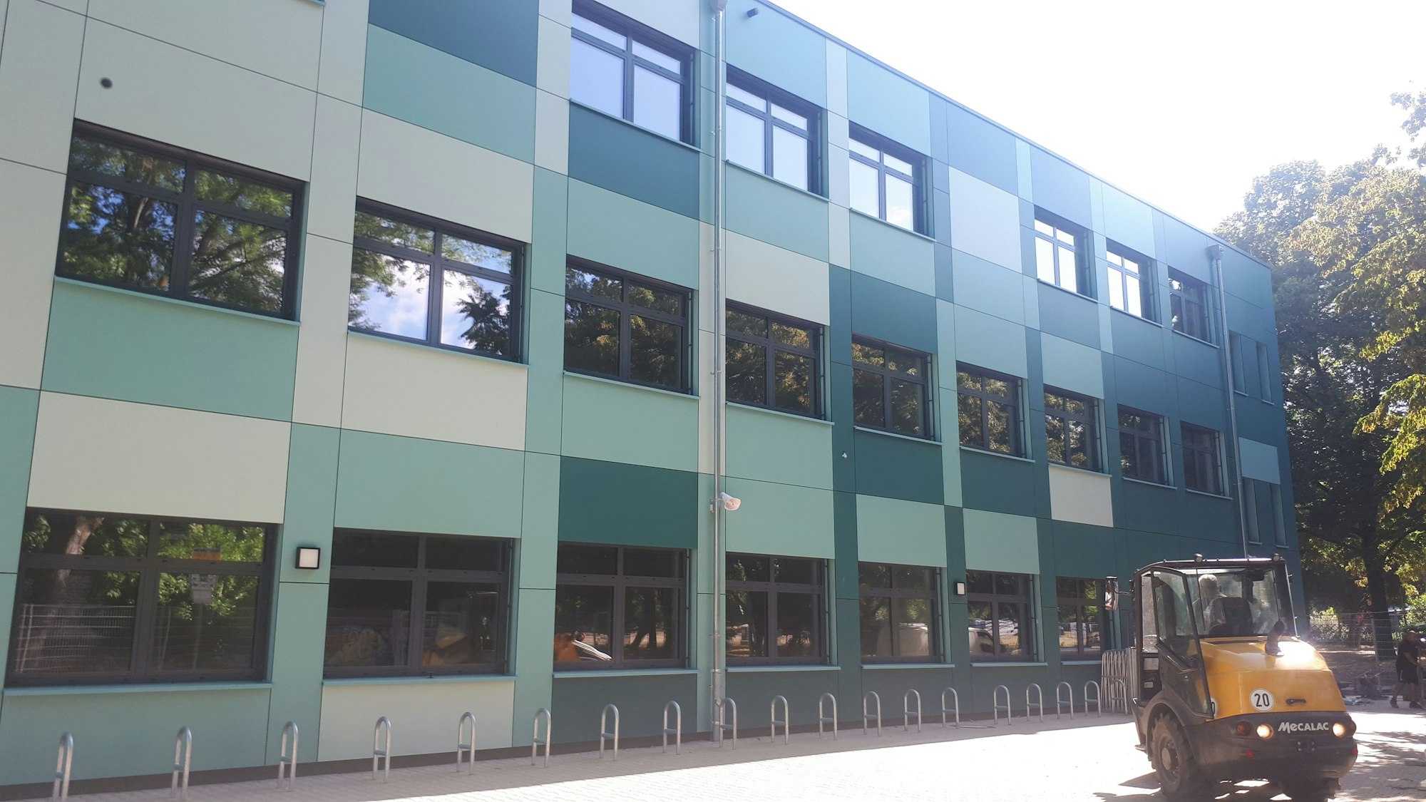 Ein grüner Schulbau mit einem Bagger davor.