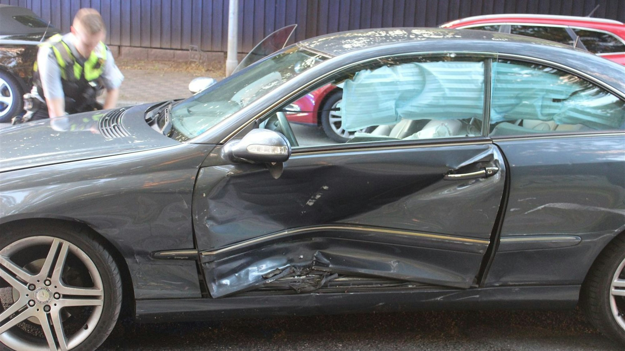 Ein Mercedes mit verbeulter Fahrertür steht auf einer Straße.