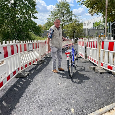 Wolfgang Sauerteig steht mit seinem Fahrrad auf einem geteerten Weg.